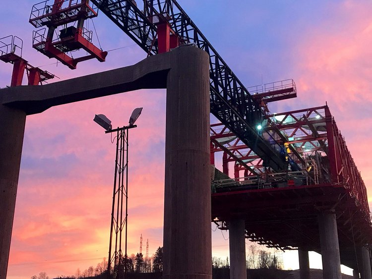 Photo: steel structure and scaffolding over newly built bridge pillars in early morning light.